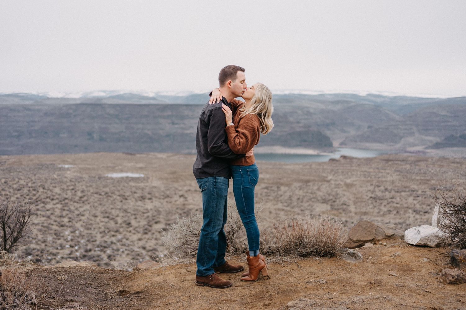 Couple embracing on cliff edge overlooking dramatic mountain landscape.