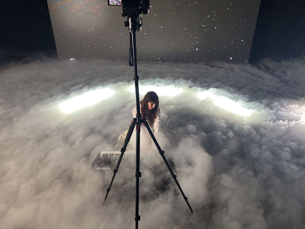 Camera tripod setup in snowy conditions at night with illuminated clouds creating atmospheric winter photography scene.