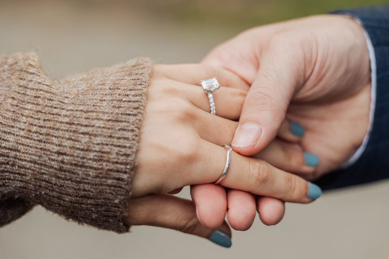 Close up of engagement ring as couple holds hands.