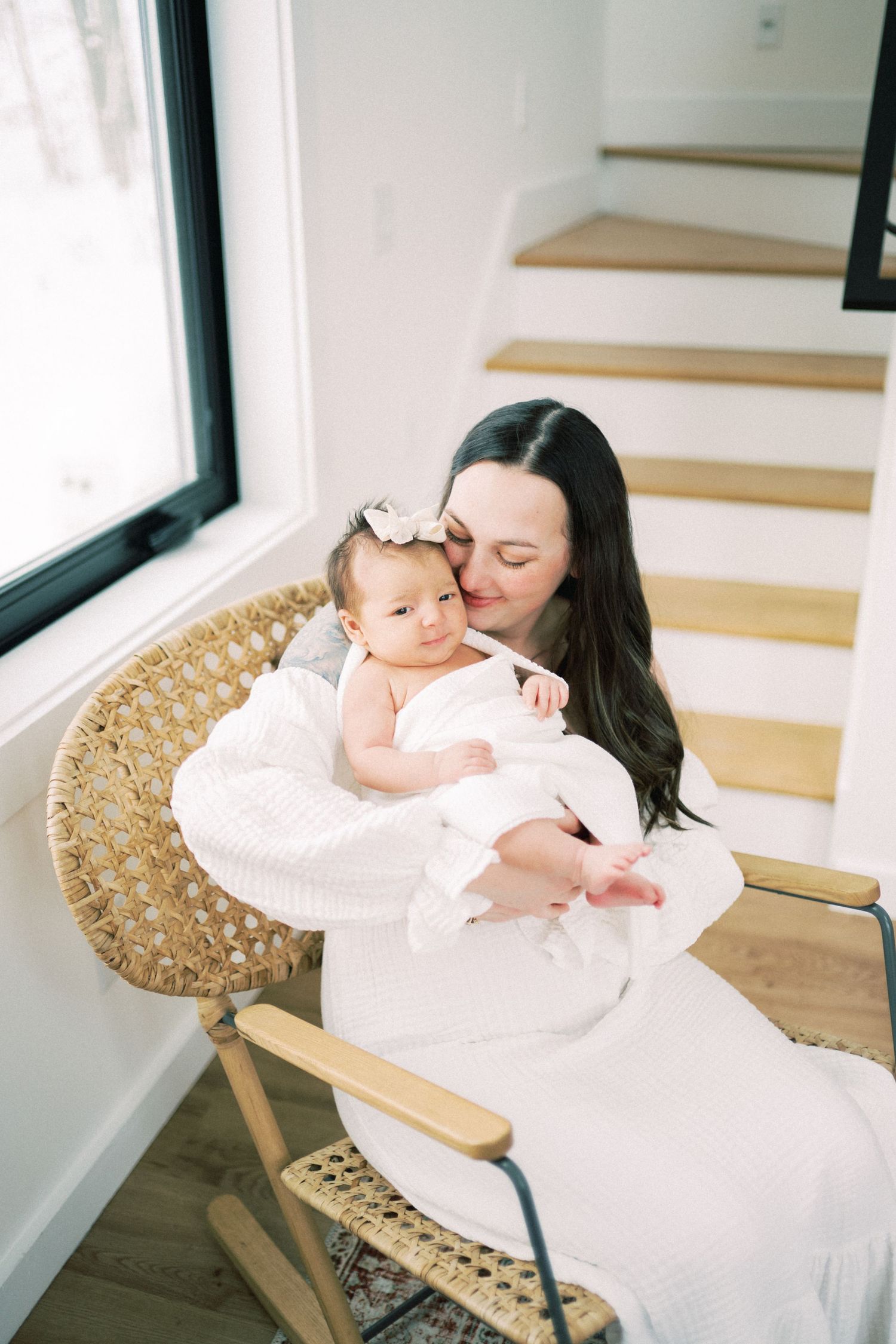 Parent and baby snuggling in wicker rocking chair by window.