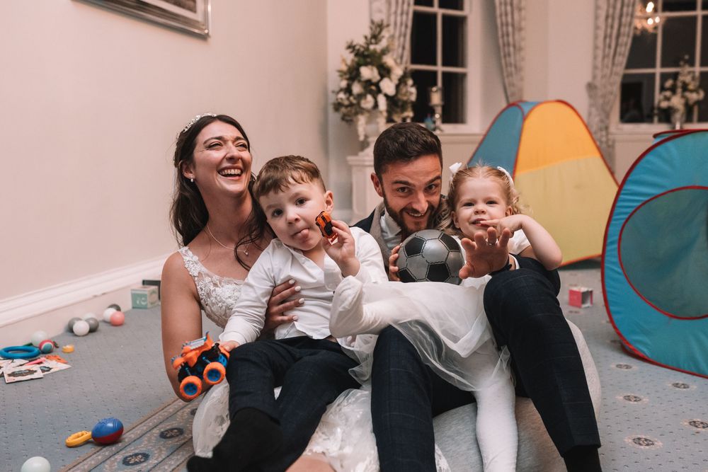 Family sitting together on floor laughing and playing in messy room with toys and tent.