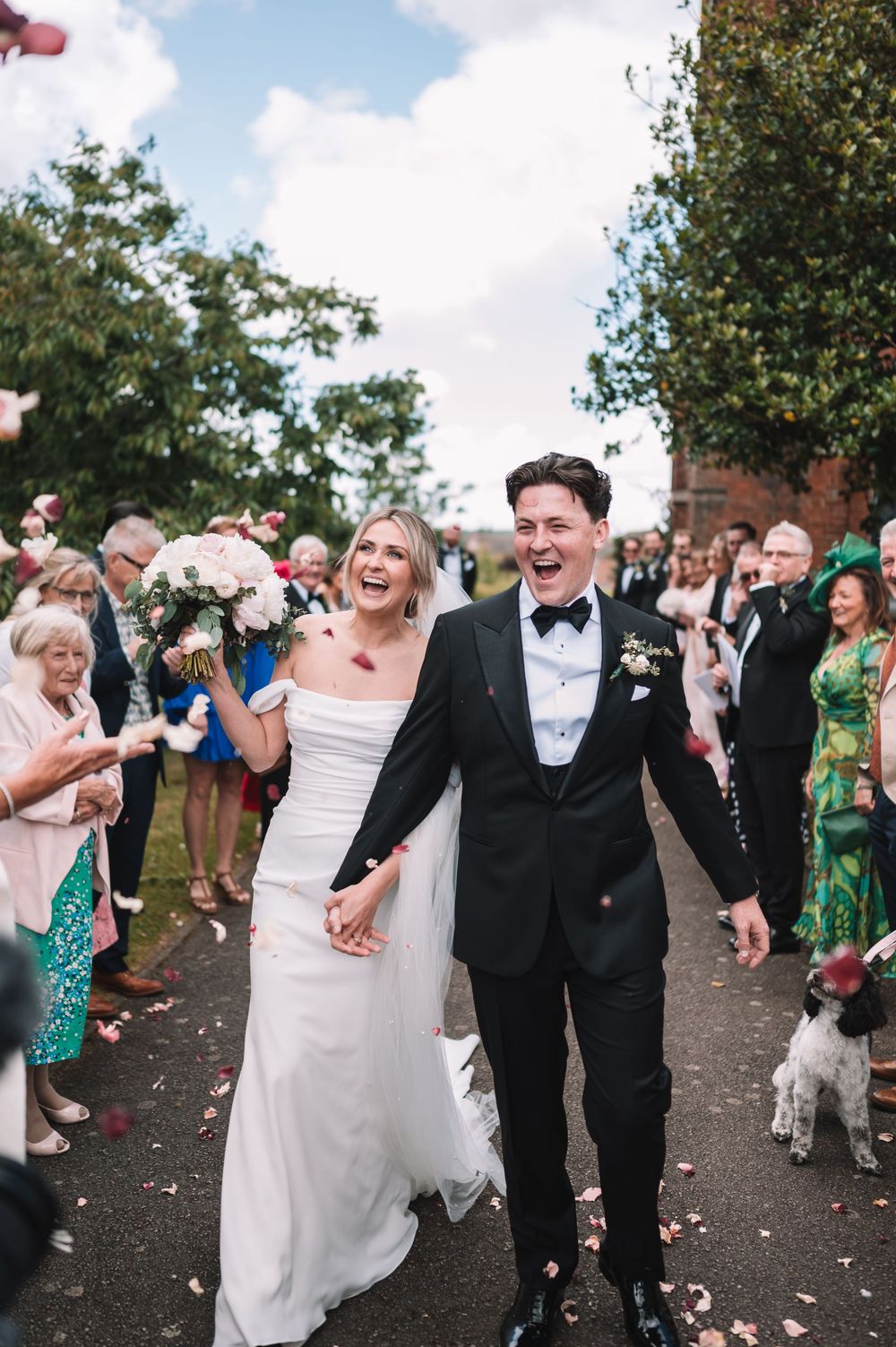 A joyful celebration at a wedding ceremony as guests throw confetti while the couple walks down the path together.