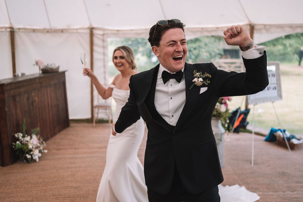 Joyful couple celebrates during their wedding reception in a white tent venue with rustic decor.