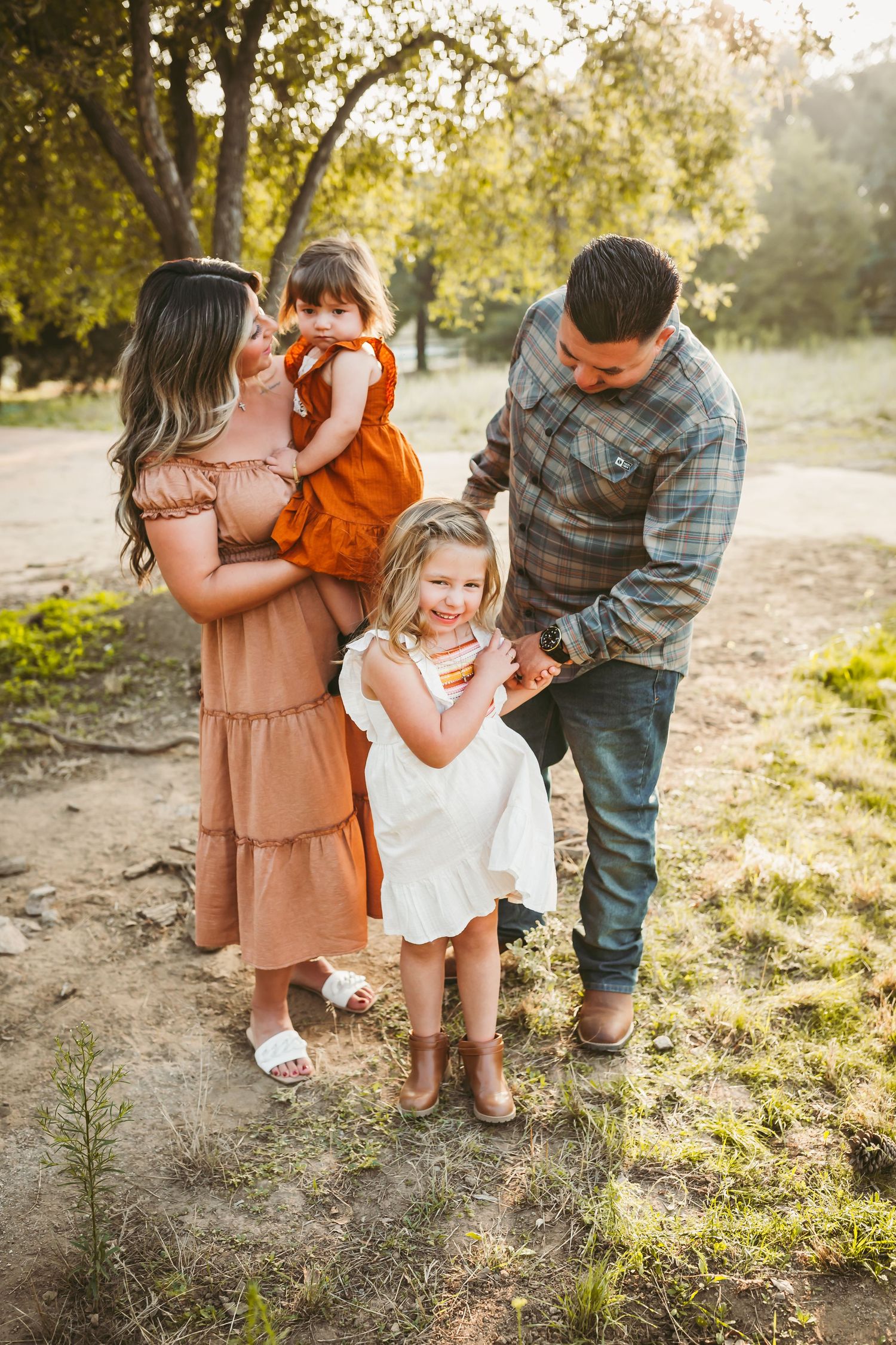 Family wearing autumn outfits playing and embracing in a sun-drenched field during golden hour.