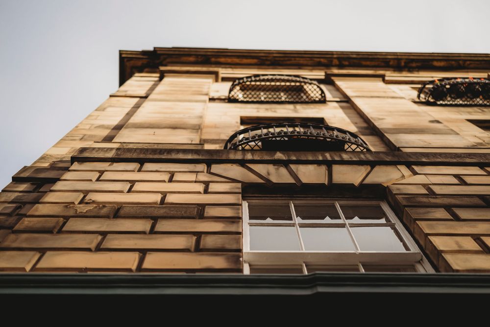 Looking up at a historic building facade with ornate window frames and beige stone walls against a dark sky.