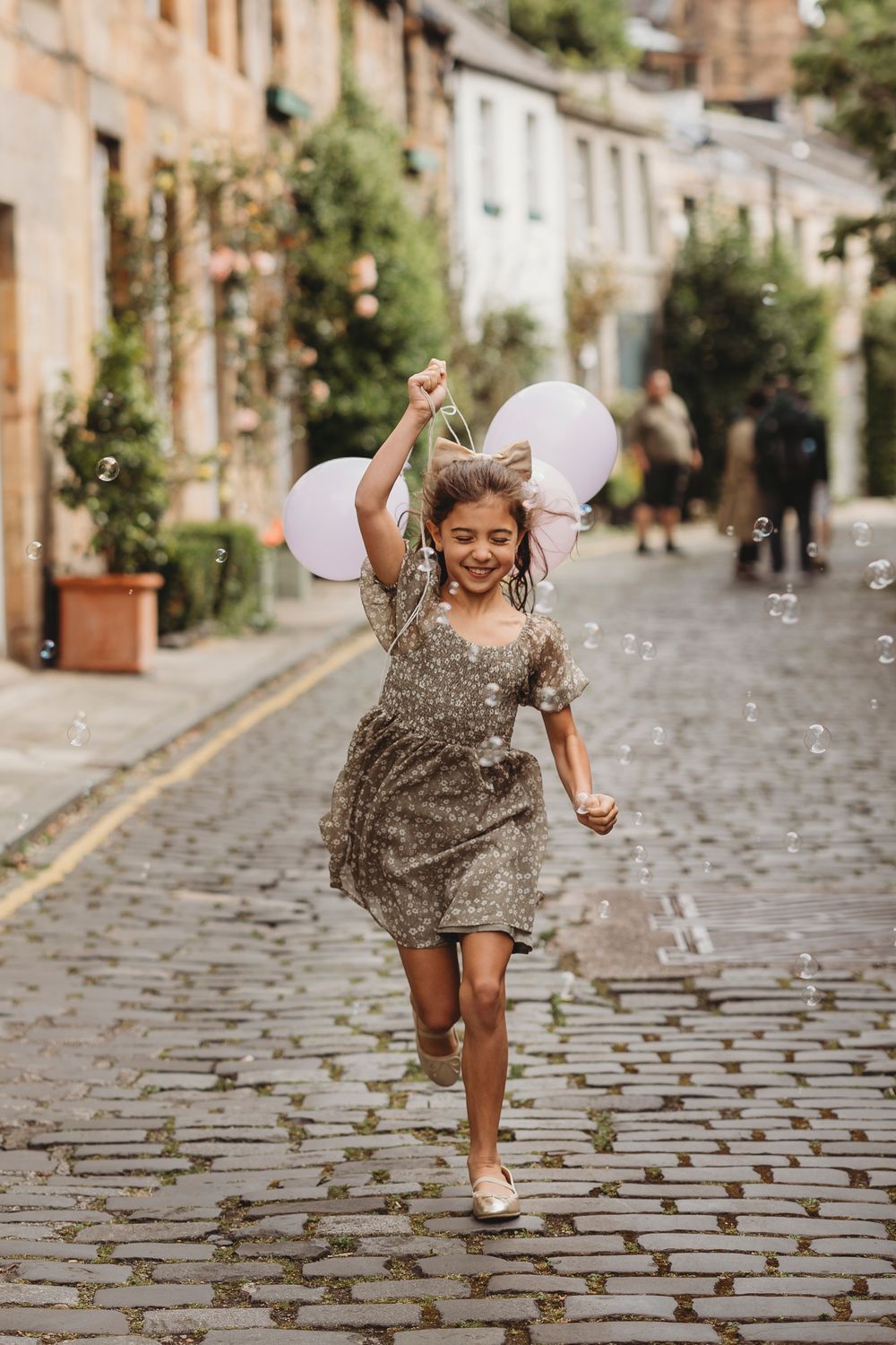 A joyful moment on a cobblestone street with white balloons and a sparkly dress against charming old buildings.