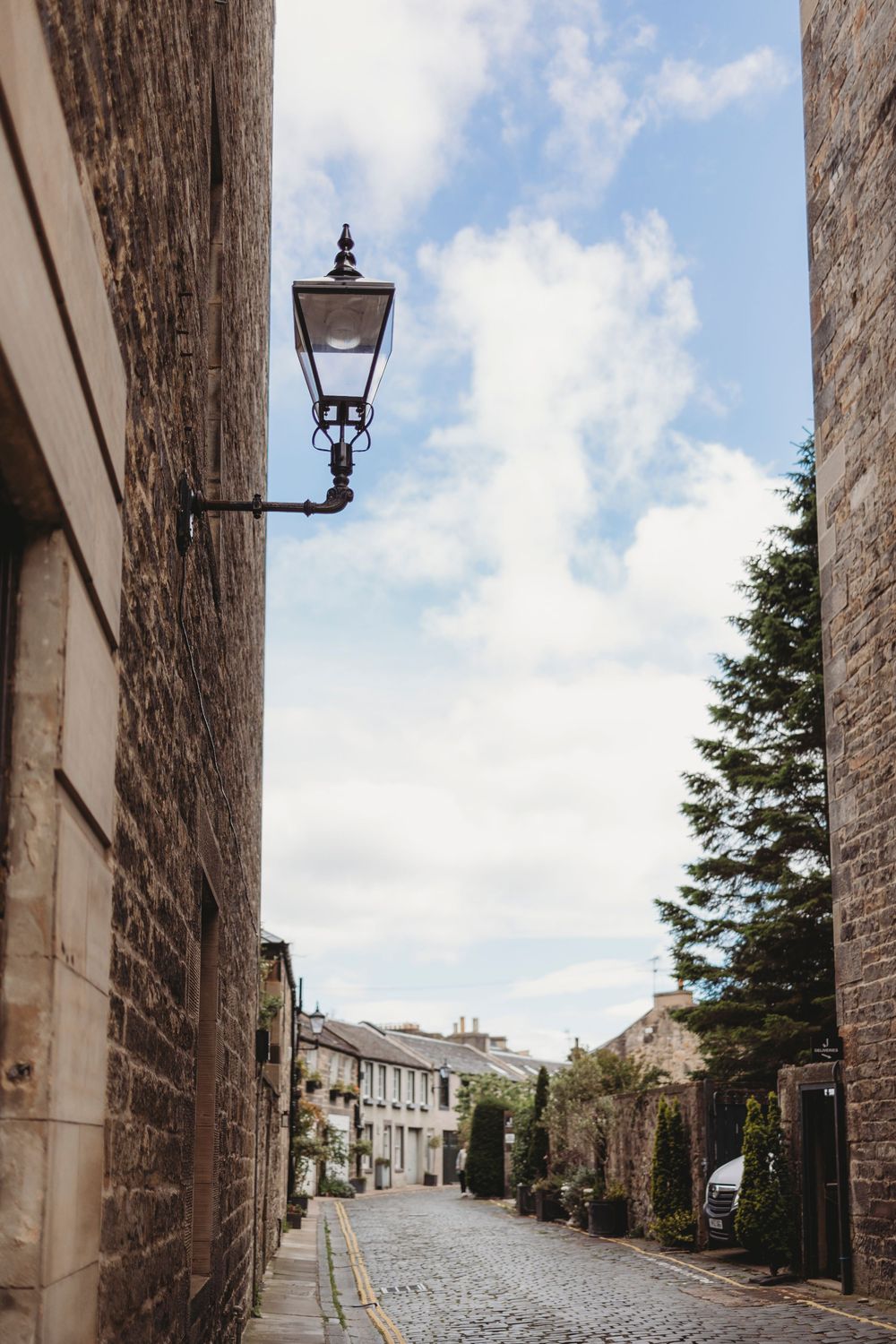 Old cobblestone street with traditional lamp post and stone buildings in a historic village on cloudy day.