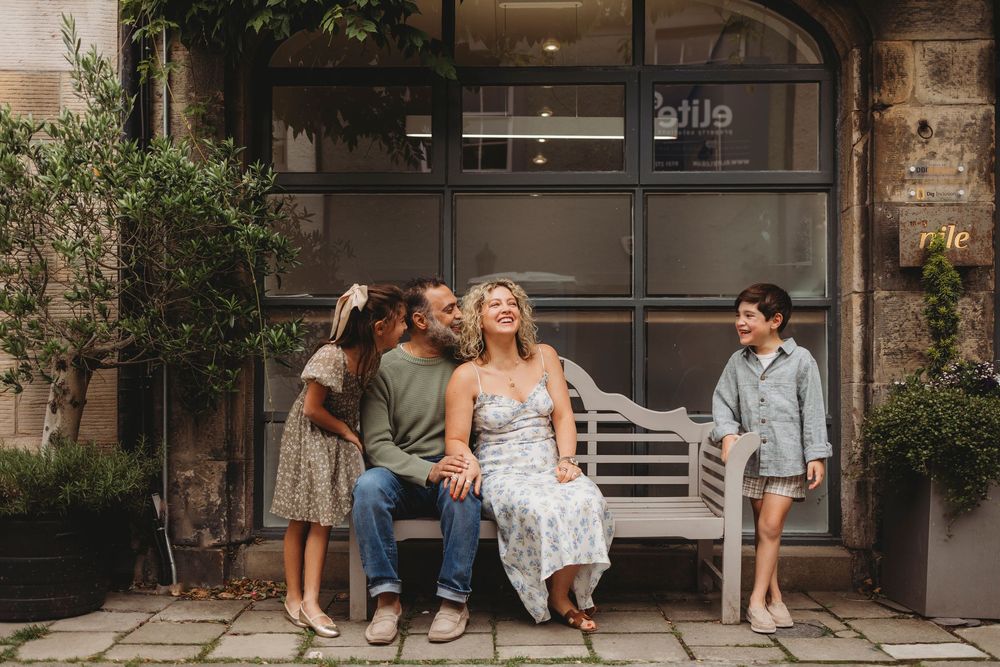 A group relaxing together on a white bench outside a storefront with glass windows and potted plants.