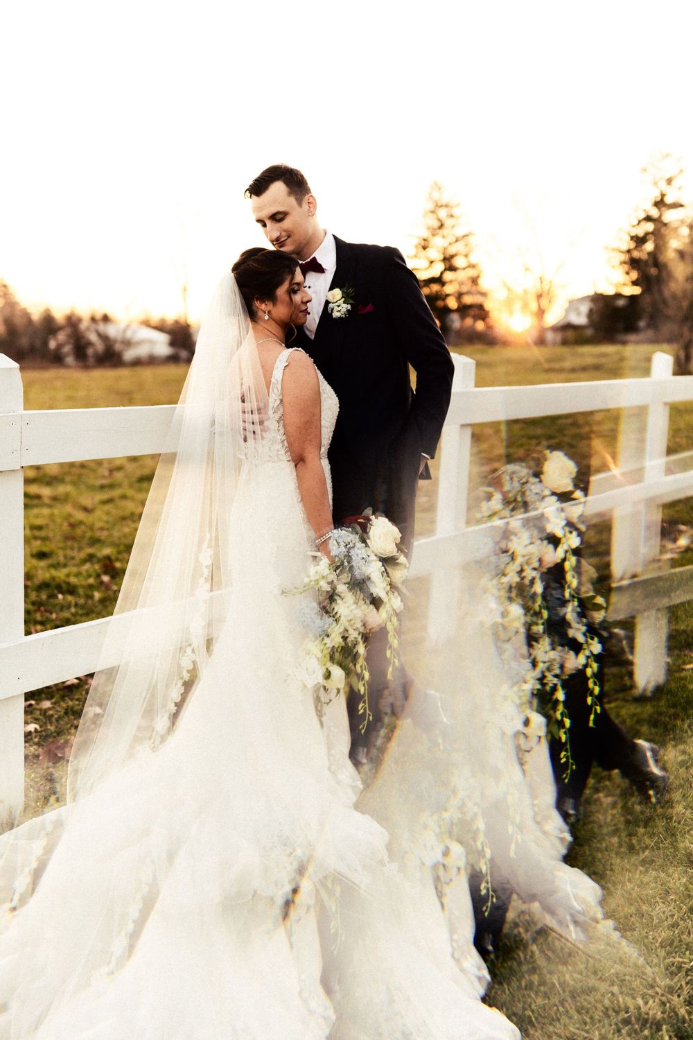 An elegant wedding portrait with a white fence backdrop during golden hour.