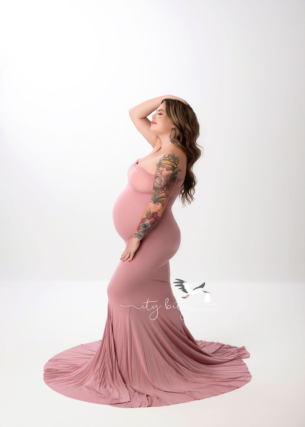 Graceful maternity photoshoot featuring a woman in a flowing dusty rose dress against a white backdrop.