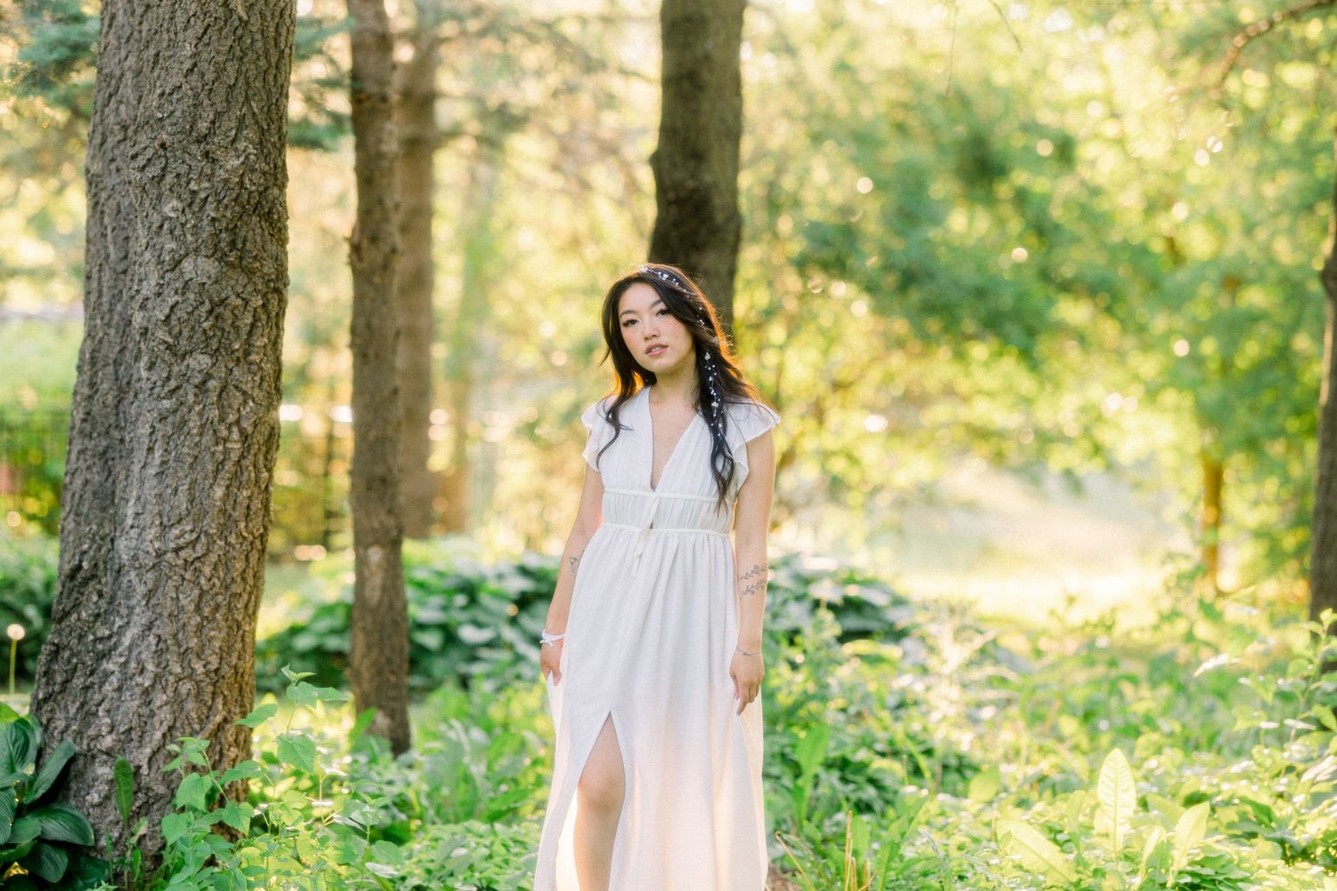A romantic portrait in a flowing white dress against a lush forest backdrop.