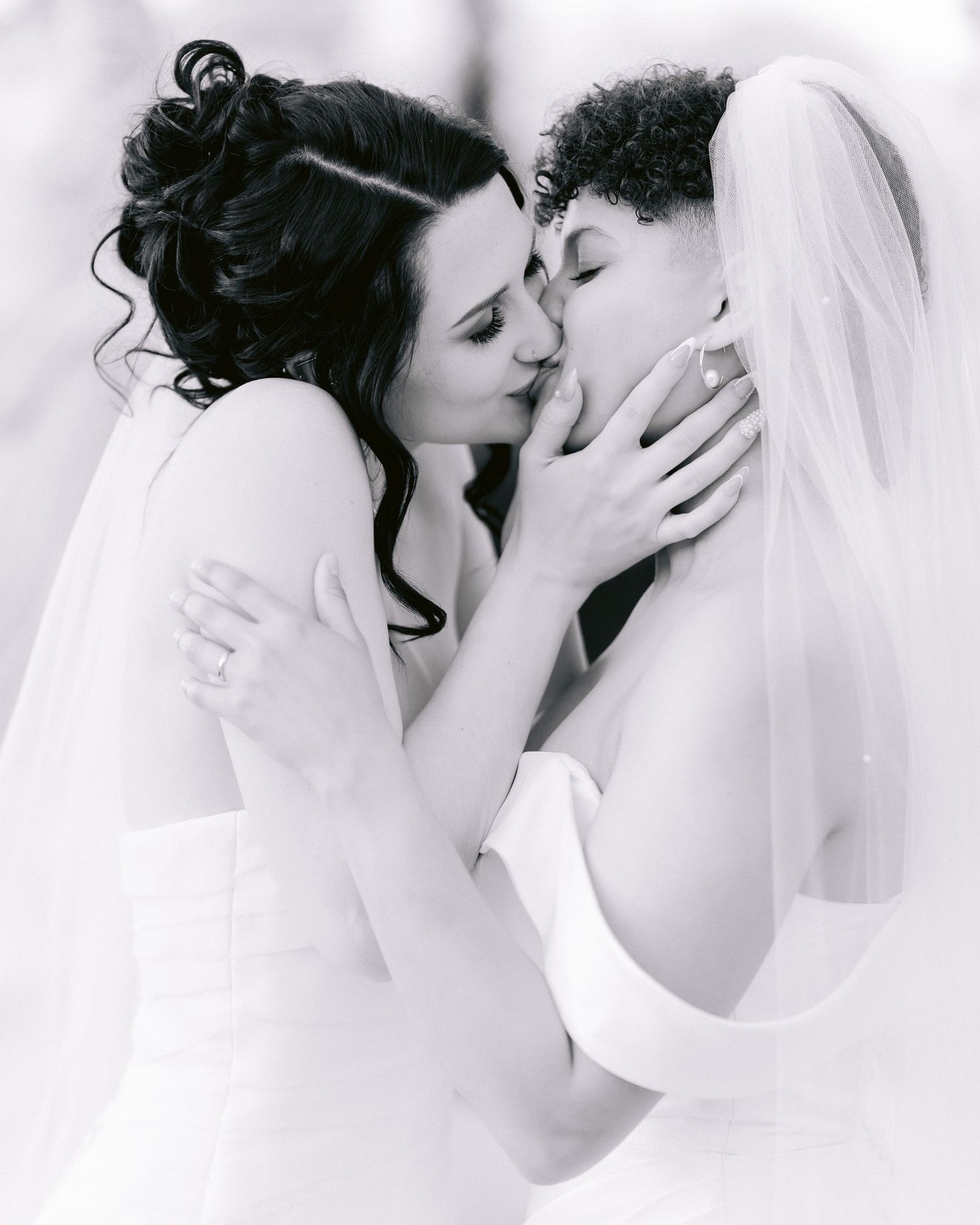 Intimate black and white photo of two brides in white dresses sharing a tender moment.