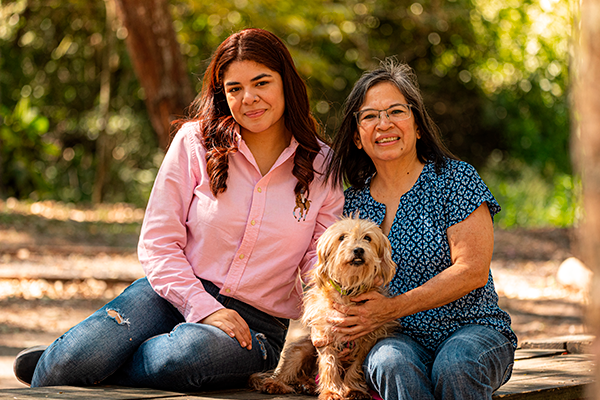 A family photo outdoors with their small fluffy dog on a sunny day.