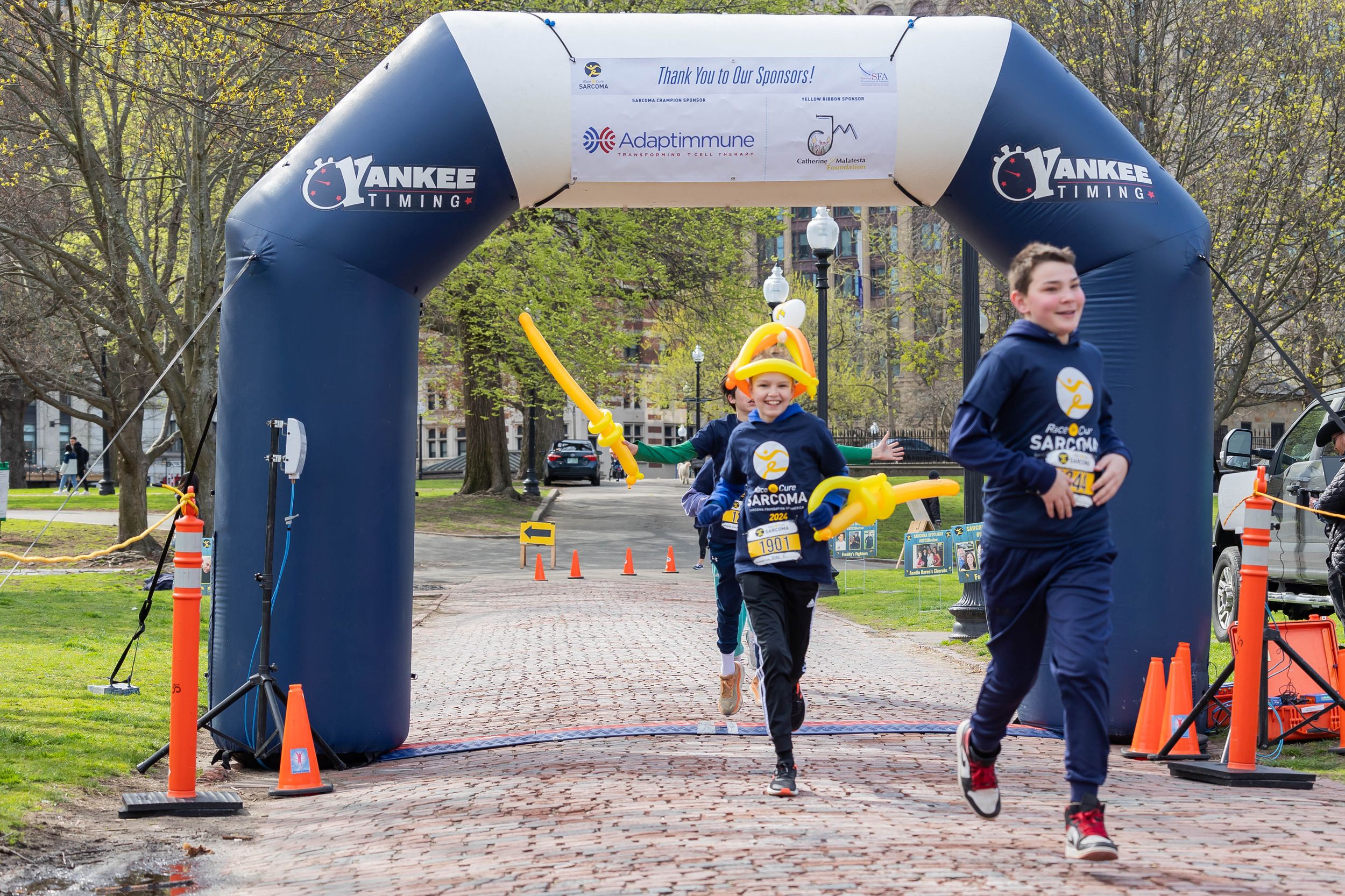 Runners passing through blue inflatable arch on brick pathway during race event.