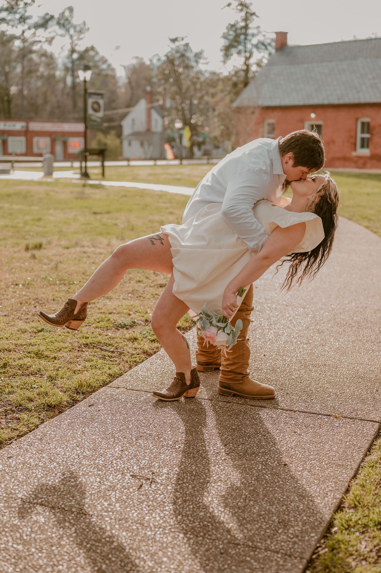 A eloping couple have a romantic dip kiss captured on a pathway with historic buildings in the background. photo by Samantha Campbell imager