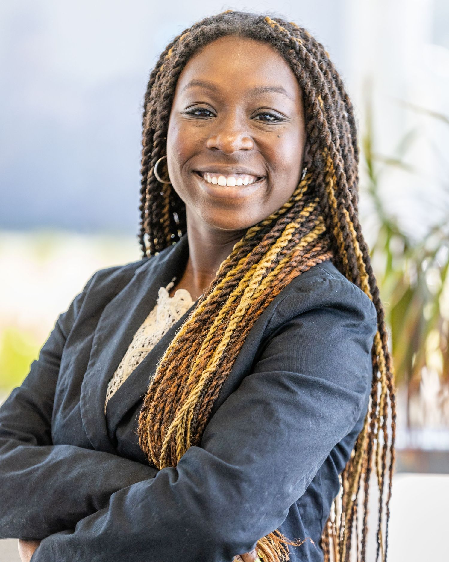Professional portrait of a smiling businesswoman in a dark blazer with long braided hair styled with golden highlights.