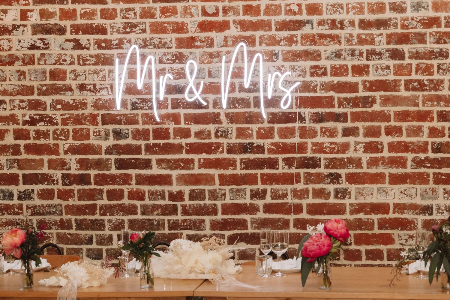 Neon 'Mr & Mrs' sign illuminates a brick wall with wedding reception table decor.