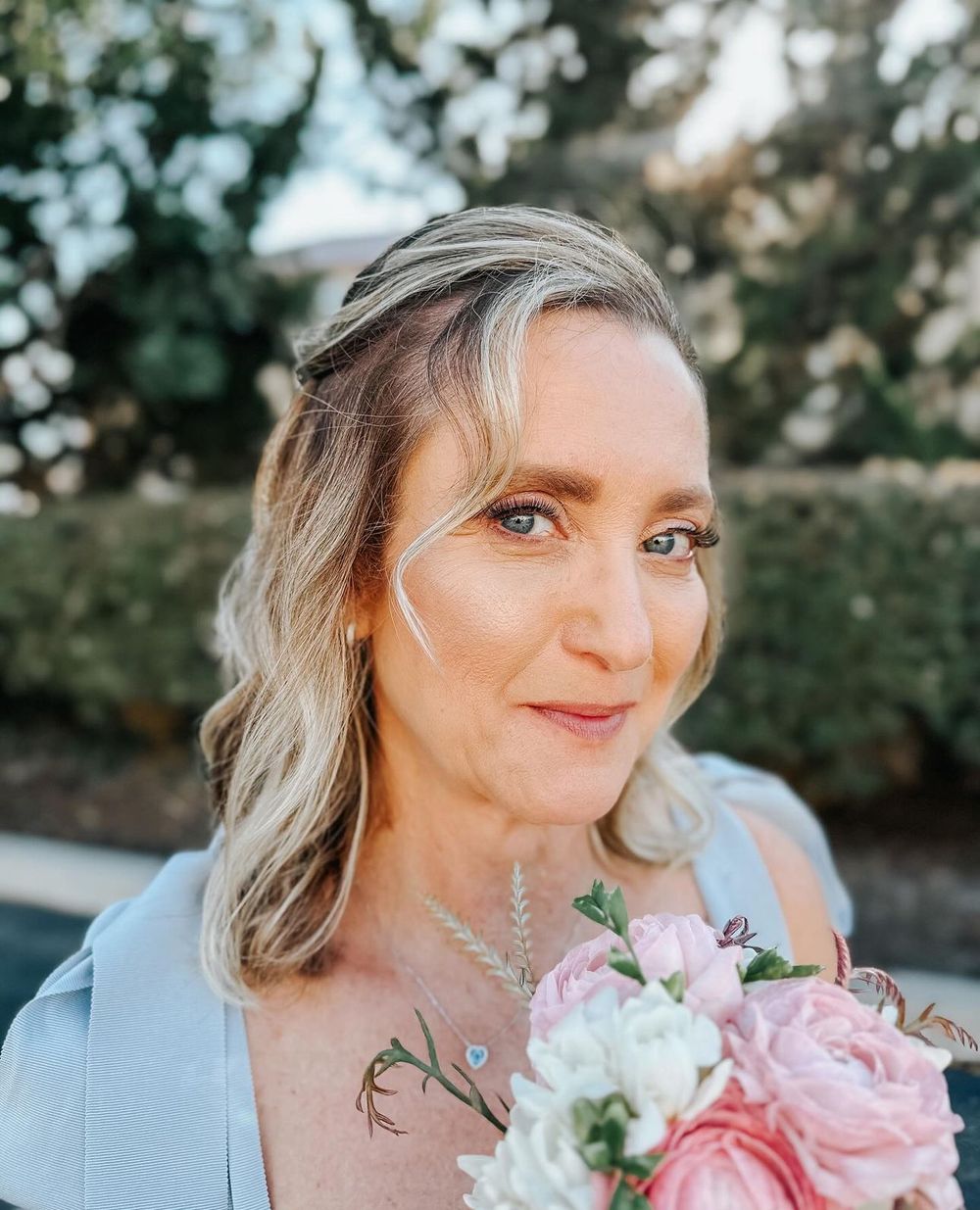 Outdoor portrait with blonde waves holding pink and white bouquet.