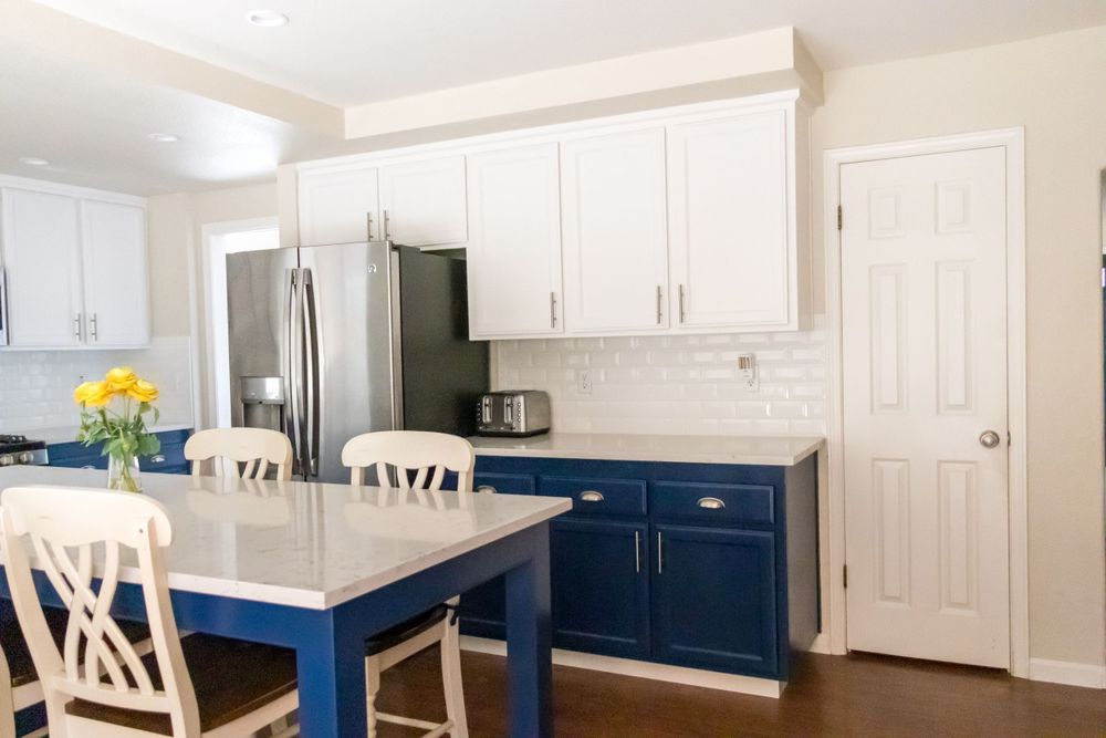 Modern kitchen with white upper cabinets, navy blue lower cabinets, and a matching blue dining table with white chairs.