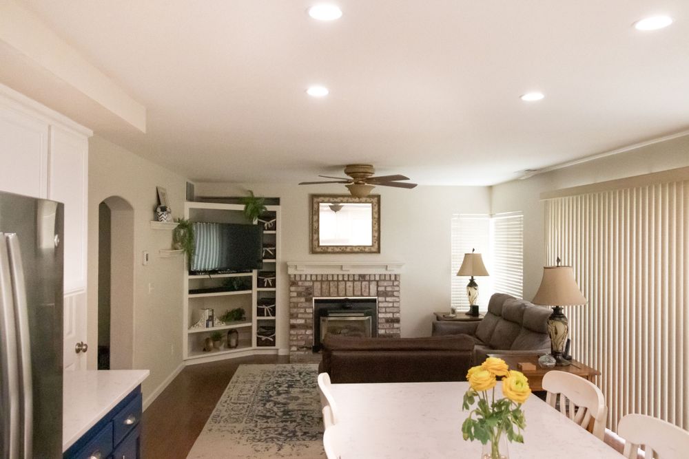 Open concept living room with brick fireplace, built-in shelving, and ceiling fan viewed from kitchen counter.
