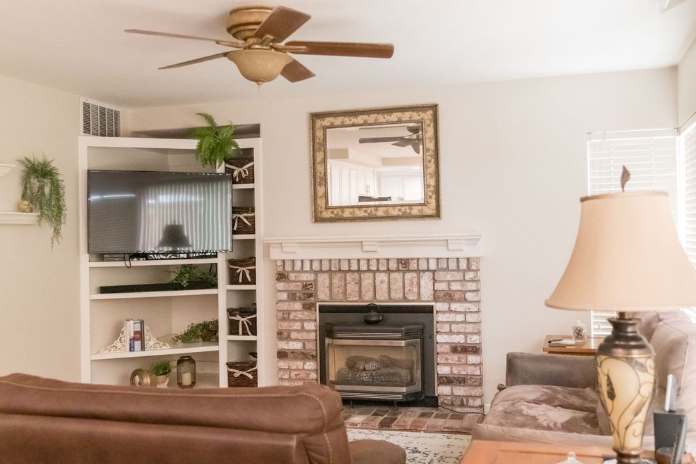 Living room interior with brown leather sofa, exposed brick fireplace, and built-in white shelving unit.