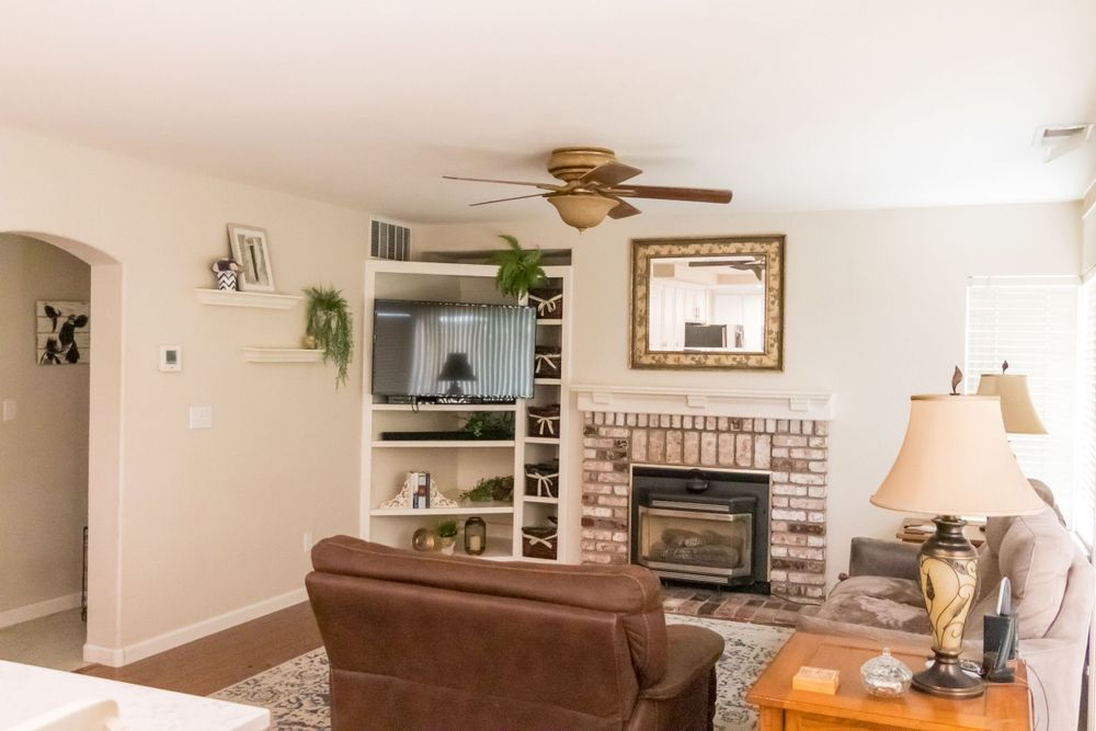 Living space with brick fireplace, wall-mounted TV, and brown leather furniture surrounded by indoor plants.