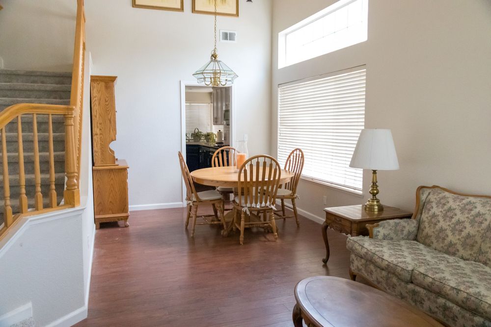 Bright dining area with wooden chairs and floral sofa, featuring high windows and hardwood floors.