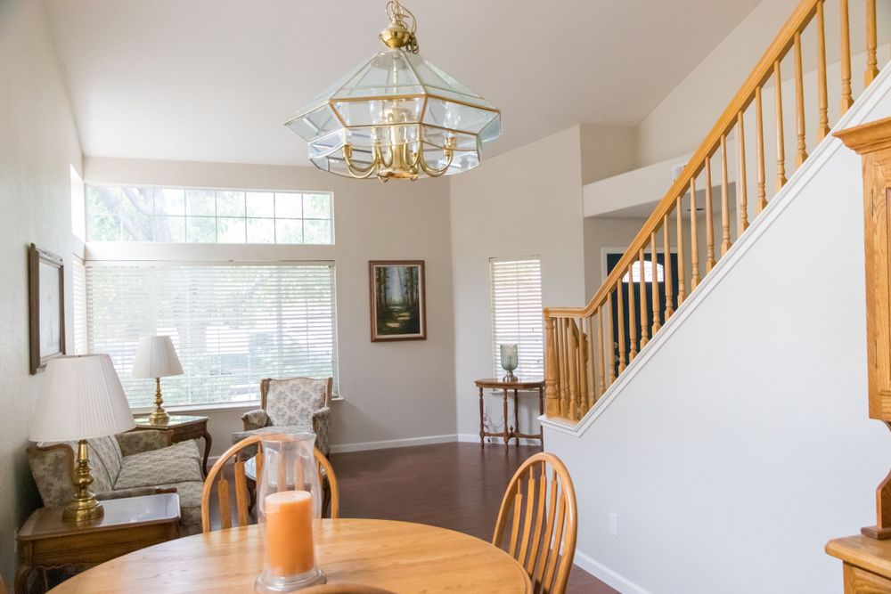 Elegant dining space with wooden Windsor chairs, brass chandelier, and oak staircase in background.