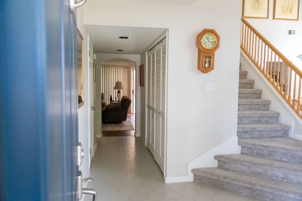 Hallway with carpet and wooden staircase featuring a vintage wall clock and cream-colored walls.