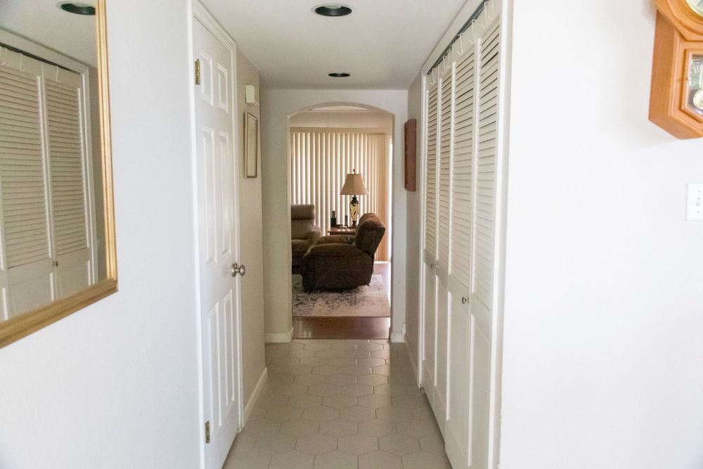 Long white hallway with closet doors and mirror leading to living area at the end.