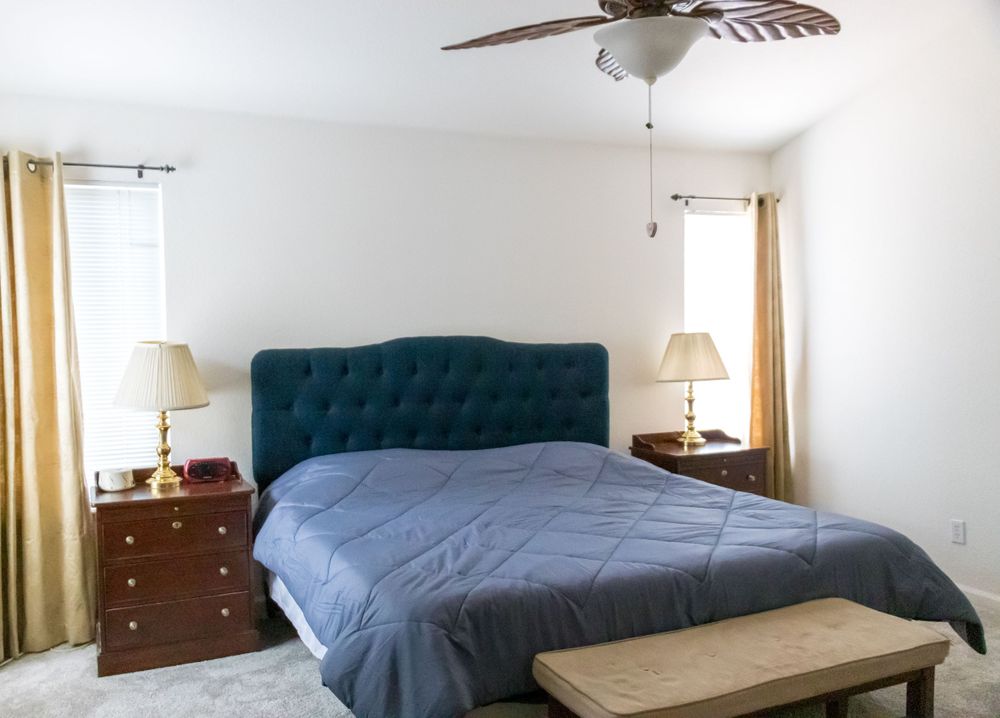 Master bedroom with navy tufted headboard, ceiling fan, and matching wooden nightstands.