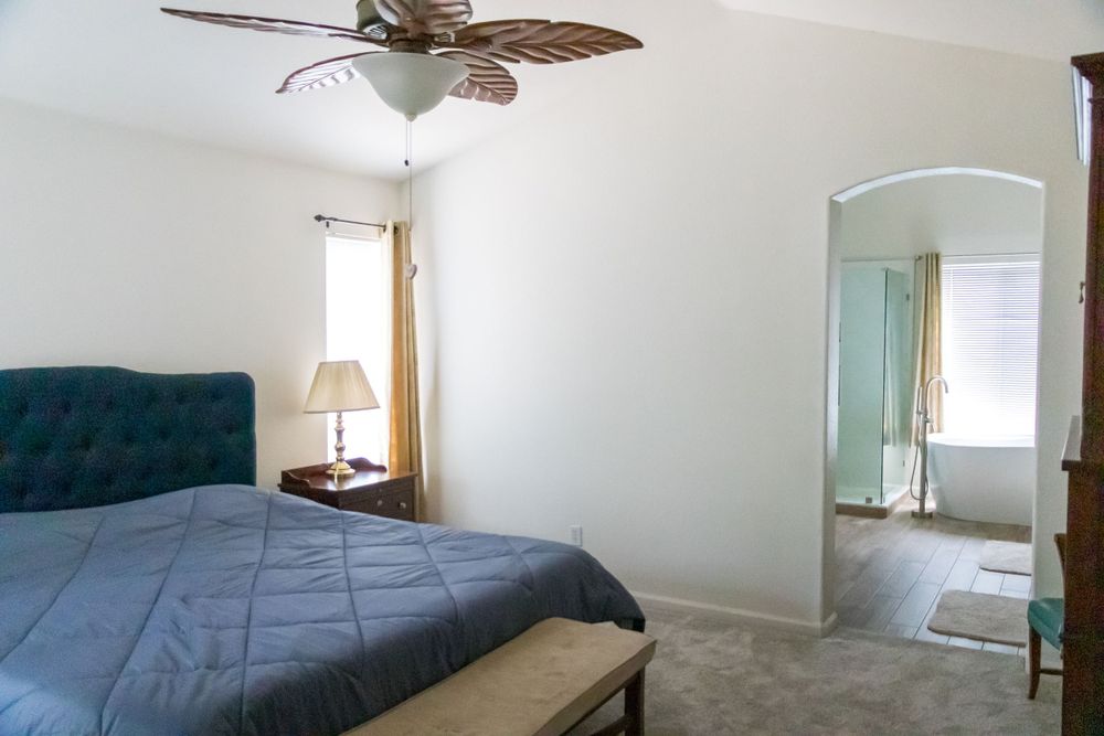 Bedroom with blue tufted bed, ceiling fan, and connecting bathroom entrance.