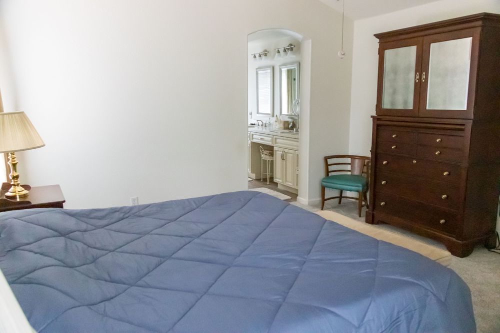 Bedroom featuring blue bedding, wooden dresser, and bathroom access.