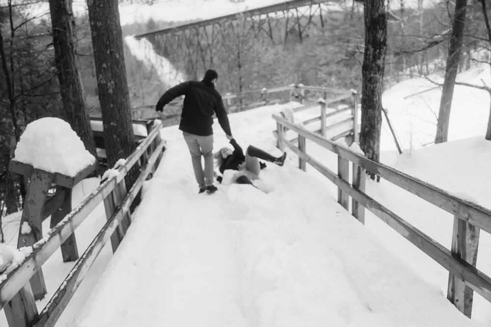 Black and white image of playful couple having fun in snow on wooden walkway.
