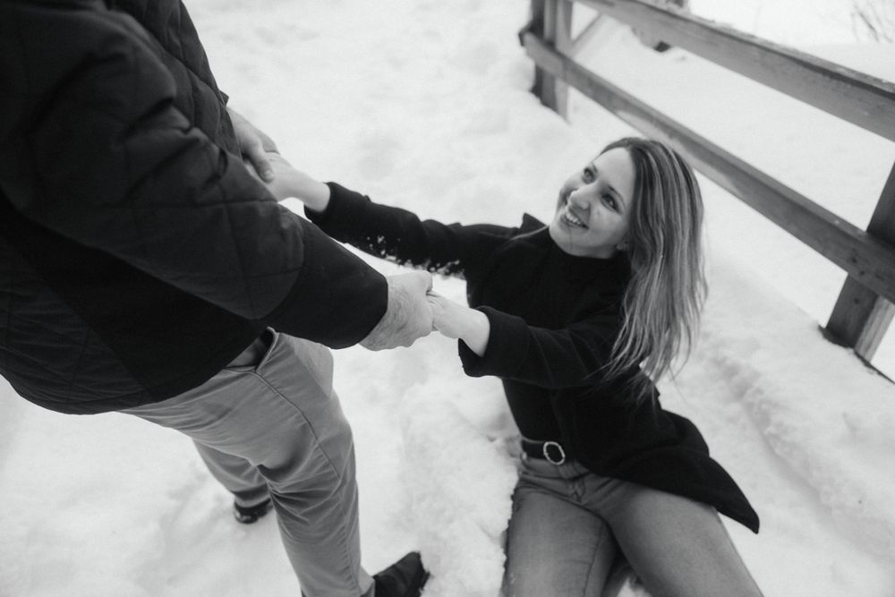 Black and white photo of couple playing in snow on wooden bridge.