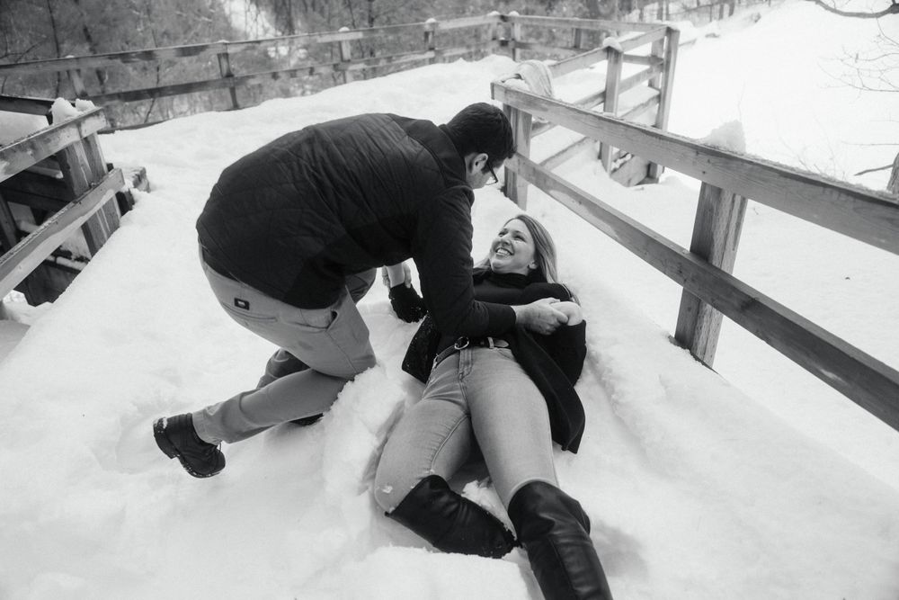 Black and white image of couple enjoying playful moment in winter snow.
