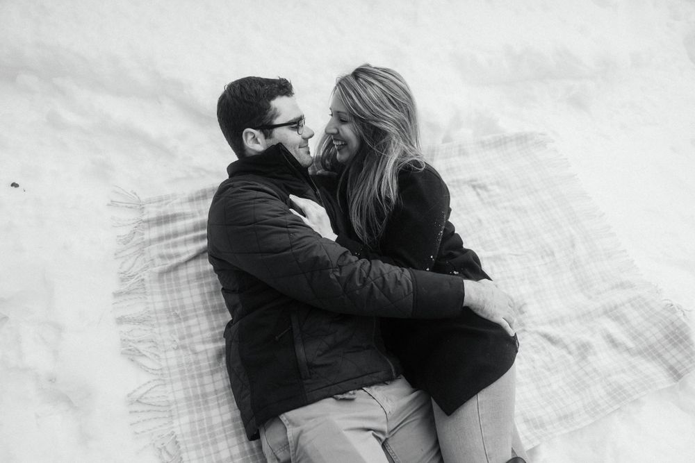 A romantic winter moment captured in black and white of a couple lying together in the snow.