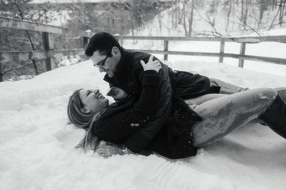 A black and white winter portrait of a couple laying in the snow during a romantic moment.
