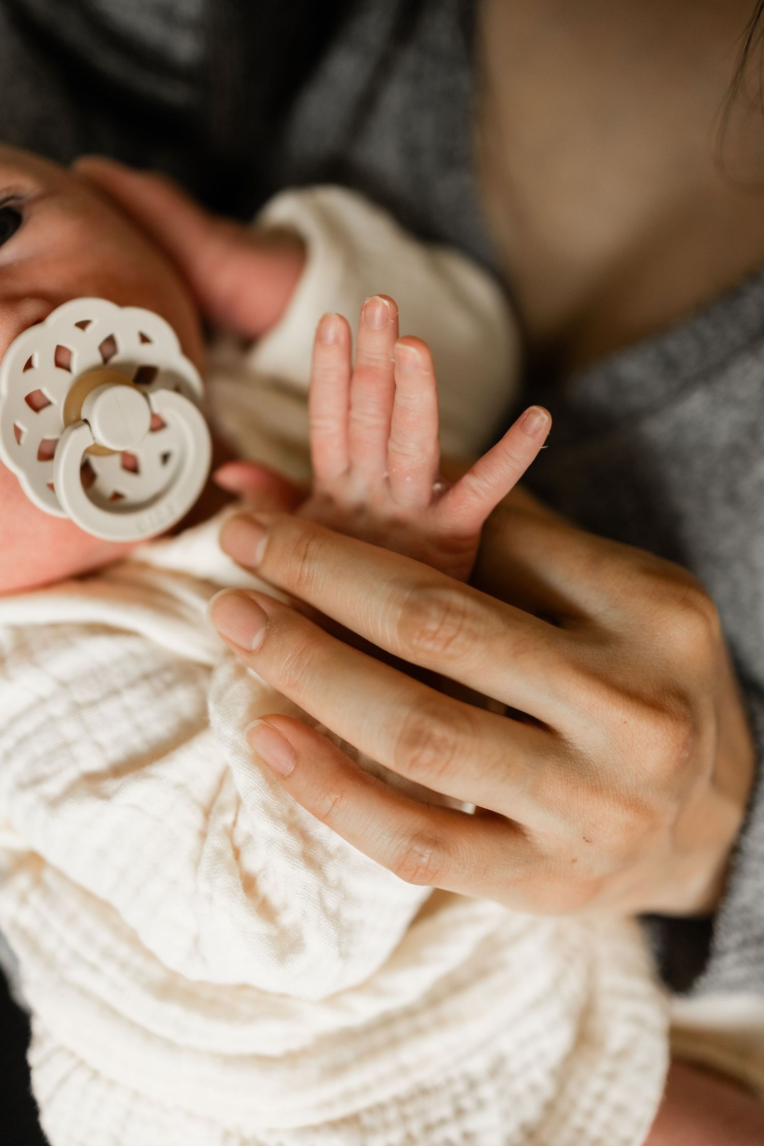 Close-up of gentle hands cradling a baby wearing white clothing with a spotted pacifier.