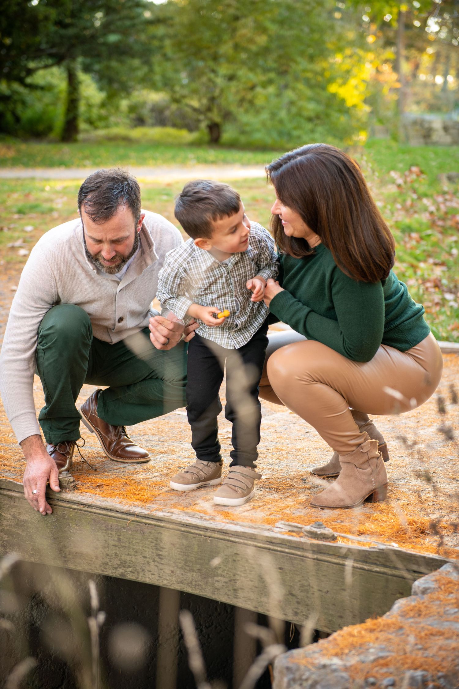 A family crouches together on a stone bridge during an autumn photo session in a park.