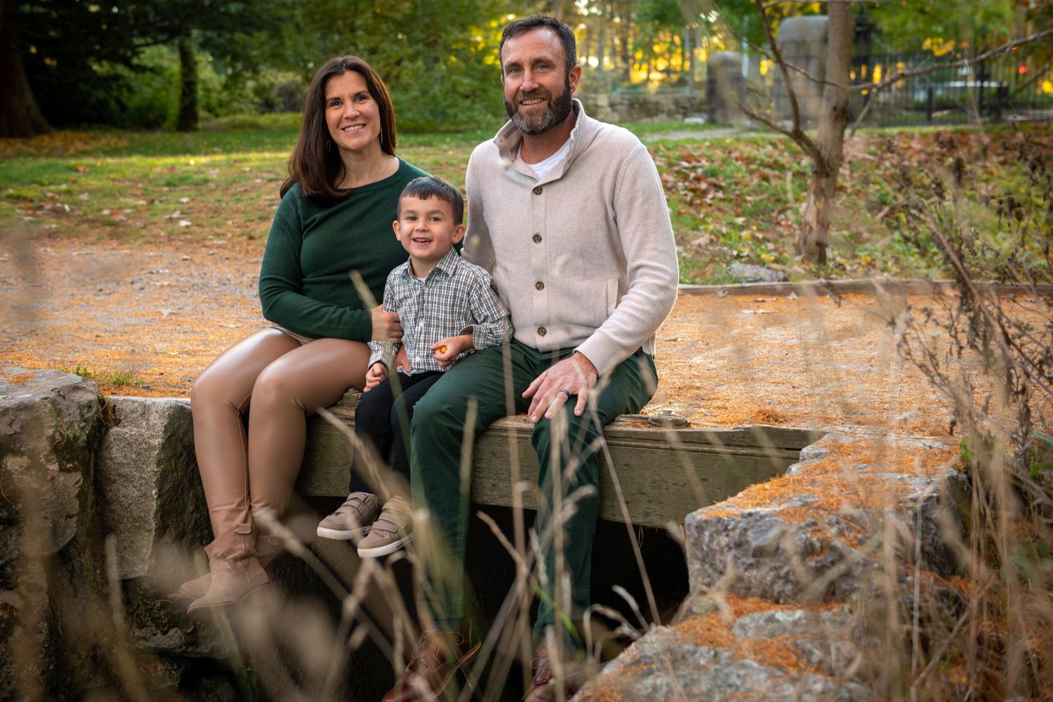 A family sitting on rustic wooden bench in an autumn park setting.