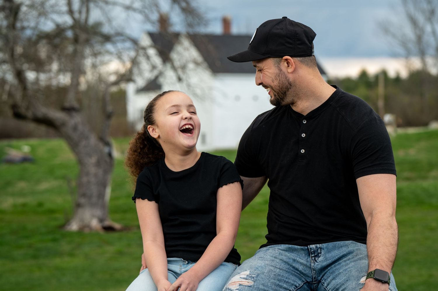 A heartwarming moment of laughter shared between daughter and dad sitting outdoors. New Hampshire Family Photography Serving New England