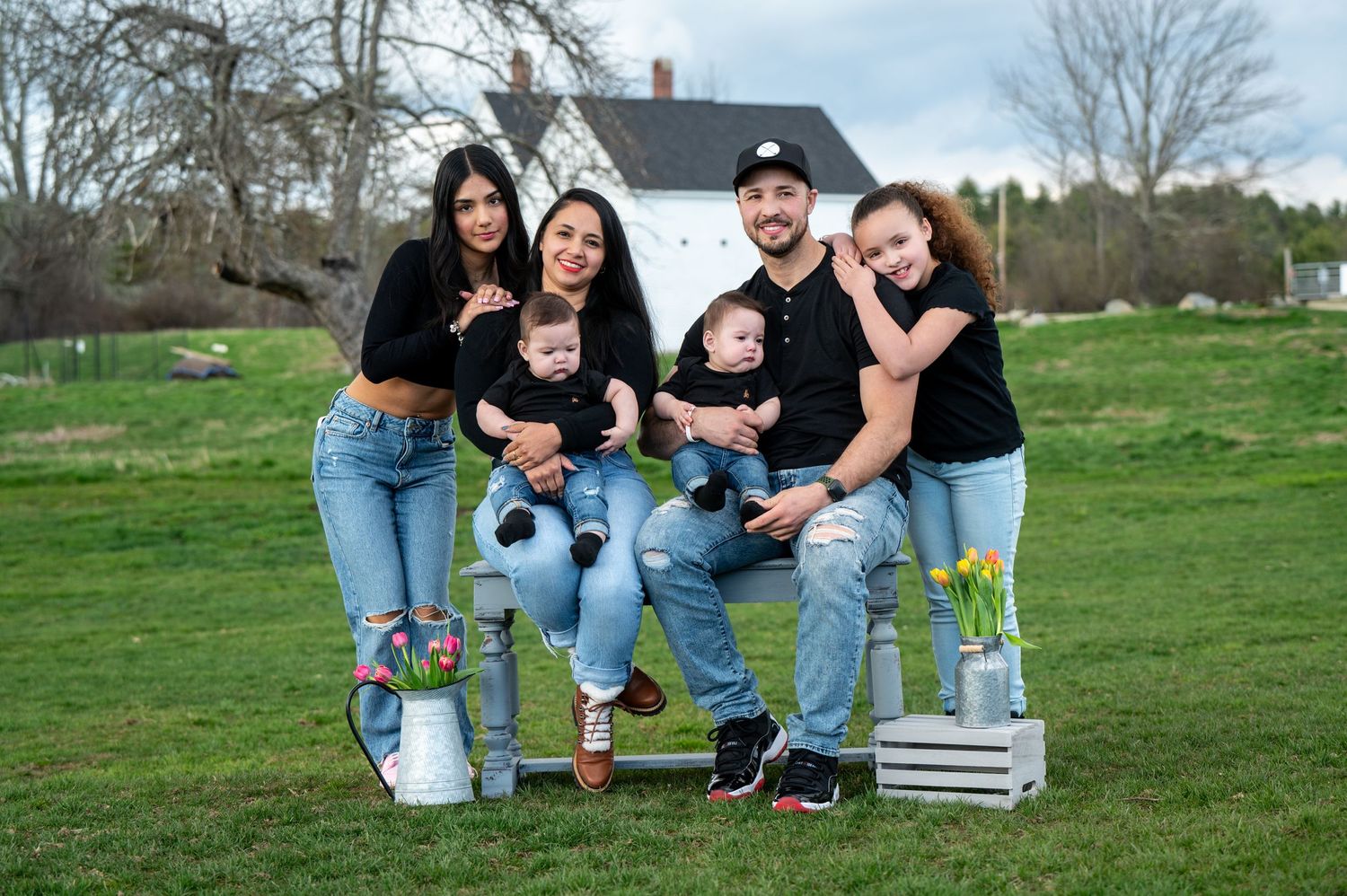 A family portrait of people sitting on wooden crates outdoors in matching black outfits. New Hampshire Family Photography Serving New