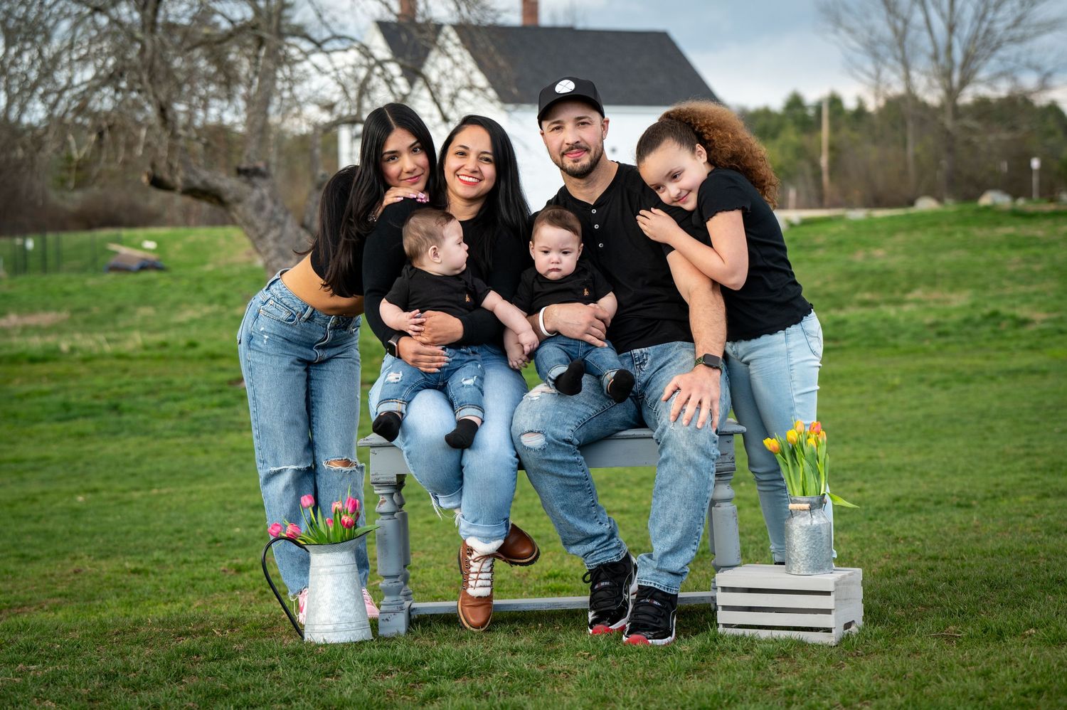 A family portrait of people in matching outfits sitting on wooden crates against a rural backdrop. New Hampshire Family Photography Serving