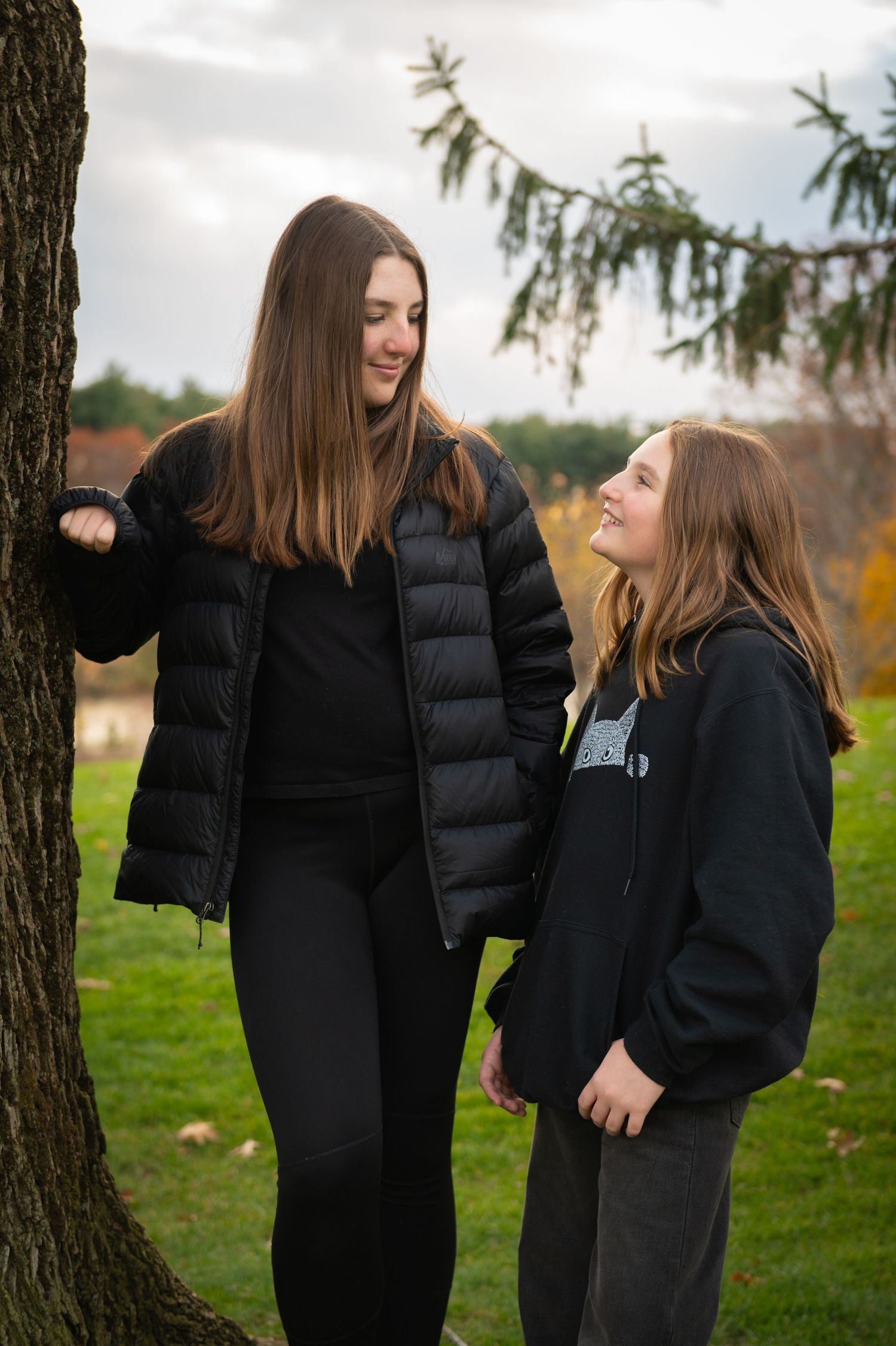 Two Sisters sharing a lighthearted moment together under a tree on a cloudy autumn day.