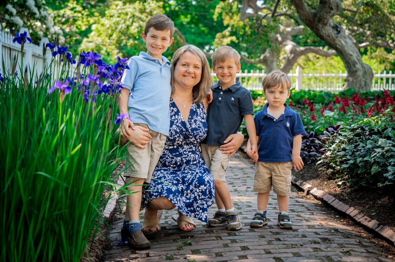 A family smiles together on a garden path with purple iris flowers in the background. New Hampshire Family Photography