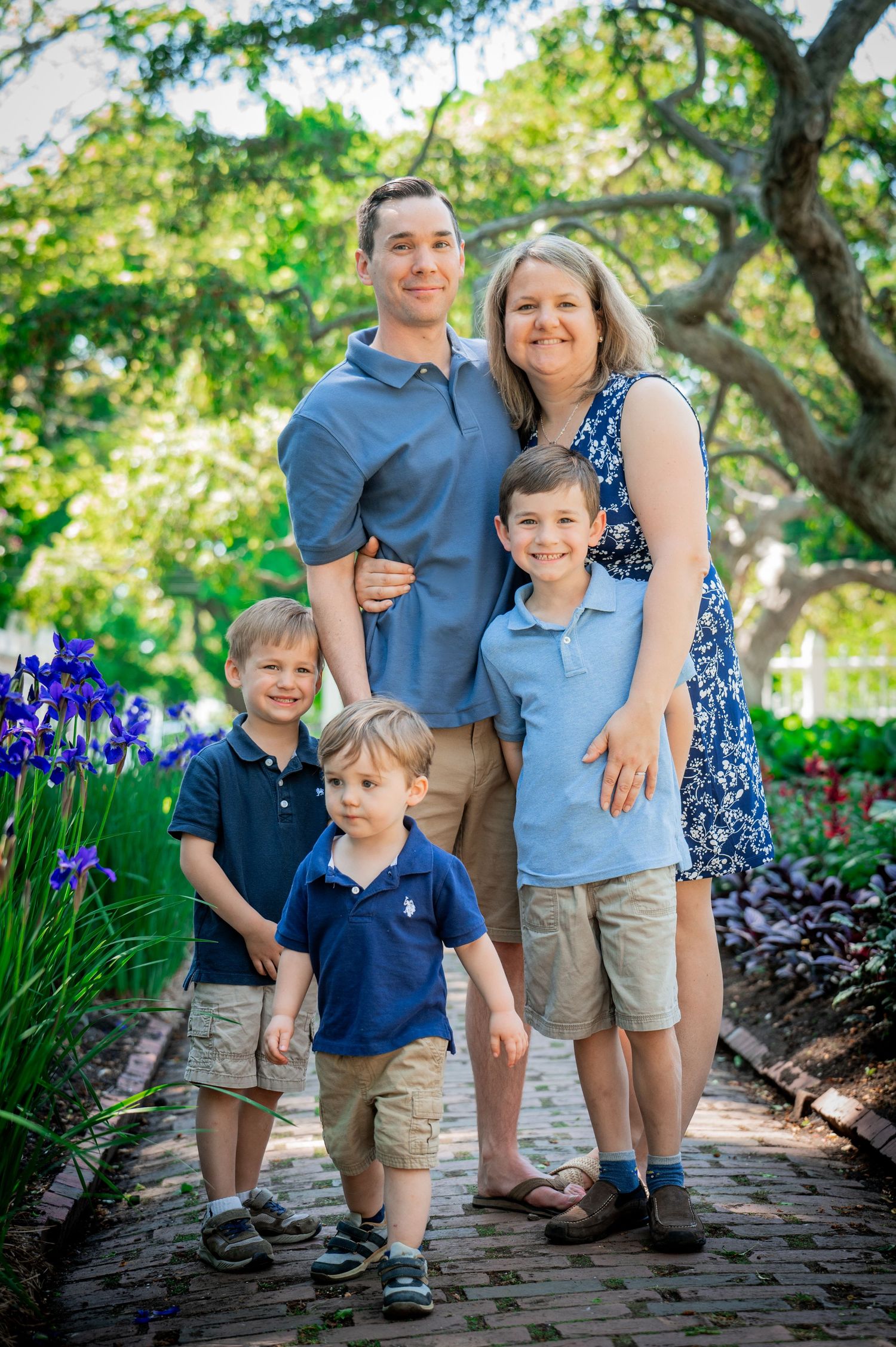 A family of five poses together on a brick path in a garden with purple iris flowers.