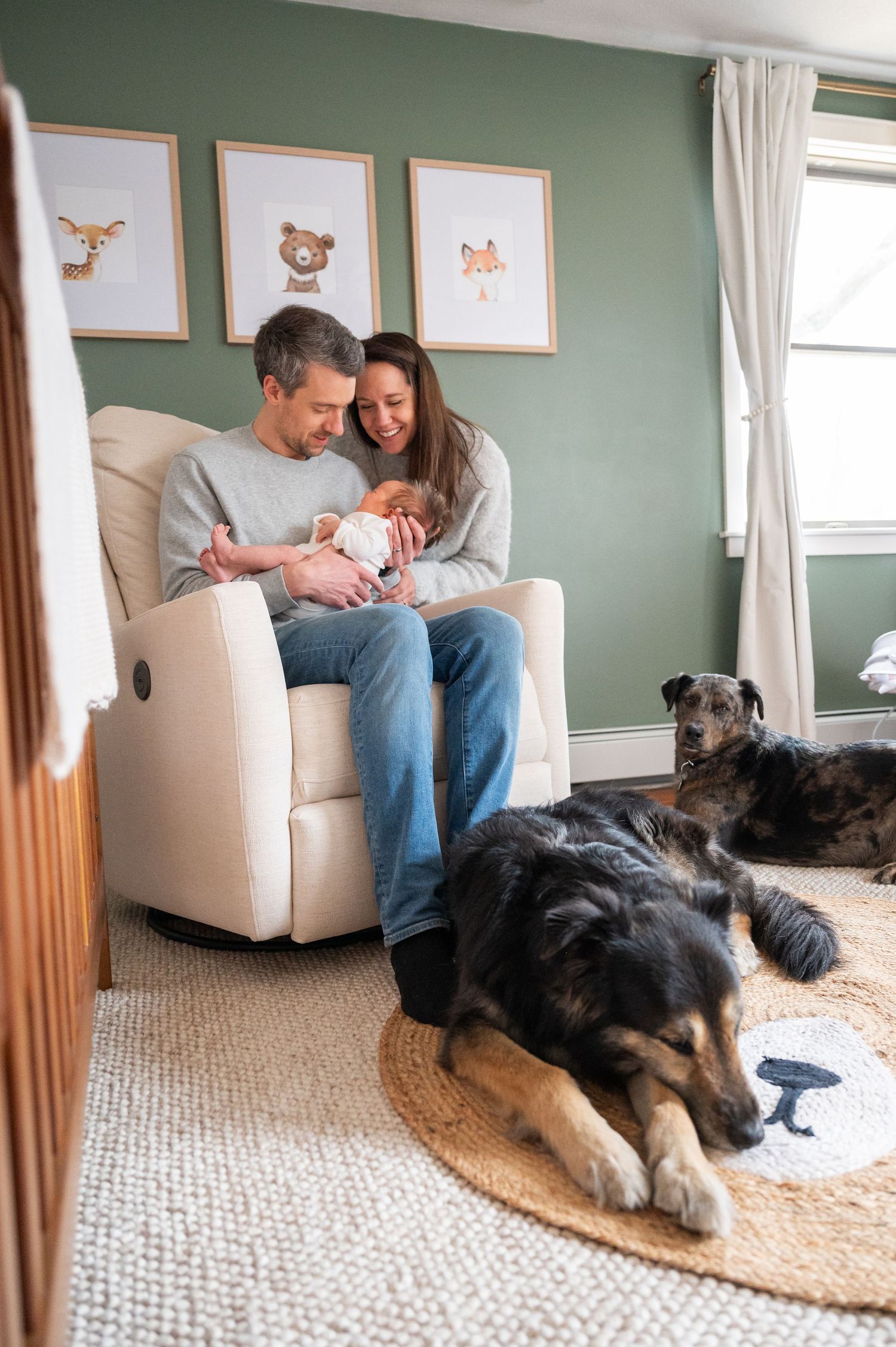 A cozy nursery scene with two dogs resting on the floor while a couple sits in a rocking chair with a baby.