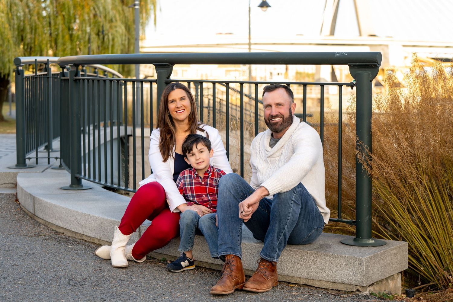 A family sits together on concrete steps at sunset near ornamental grasses and a metal railing.
