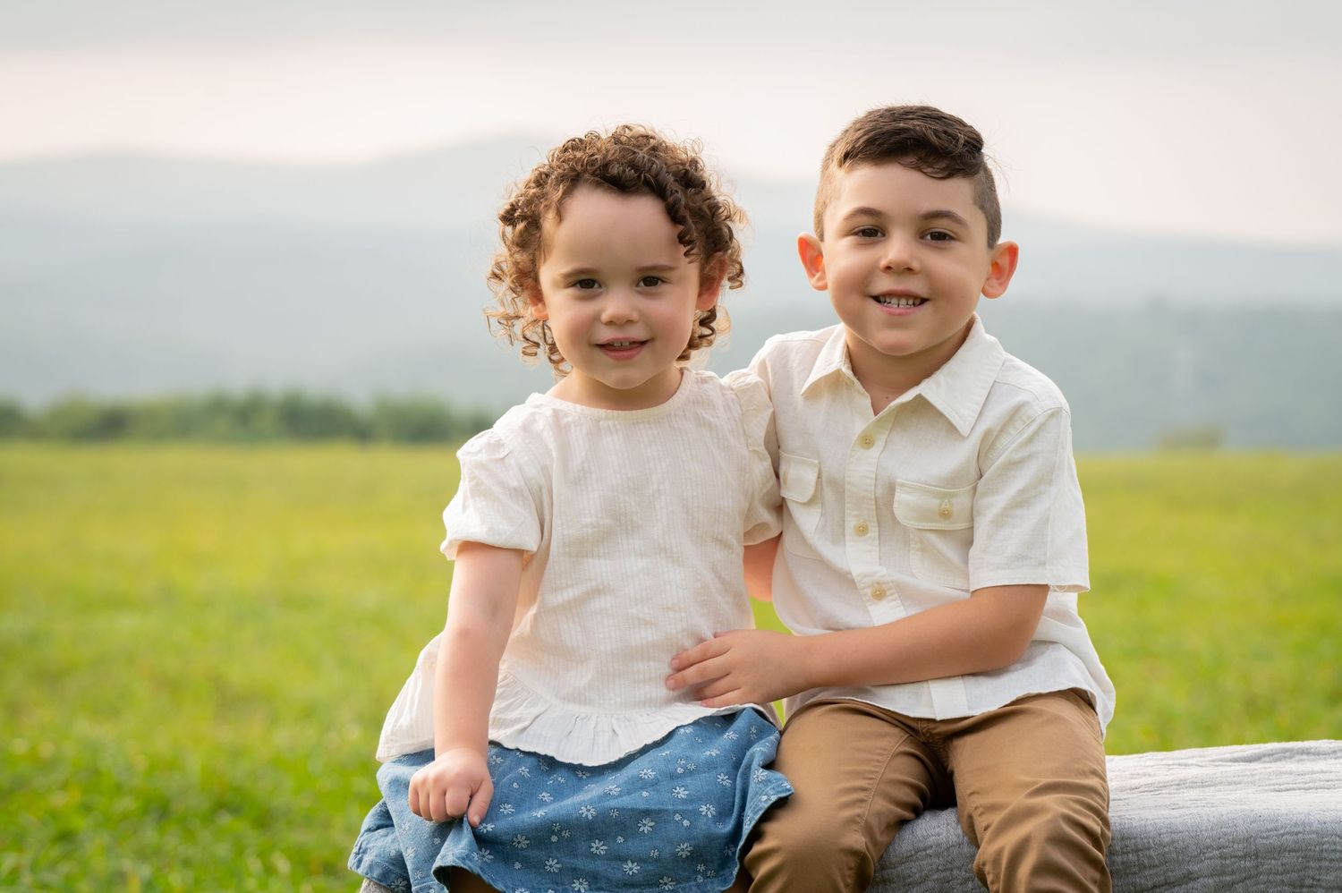 Two young children sit together on a wooden fence with mountains in the background. New Hampshire Family Photography Serving New England